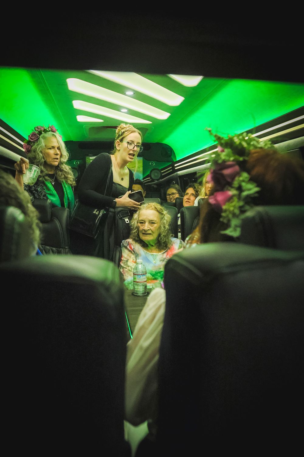Passengers in dark interior of vehicle illuminated by bright green overhead lighting creating an eerie atmosphere.
