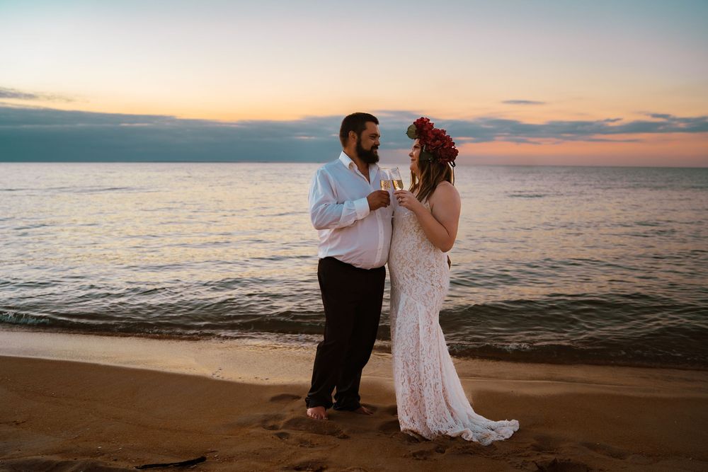 A couple dancing together on the beach at sunset in Hawaii while wearing formal wedding attire.