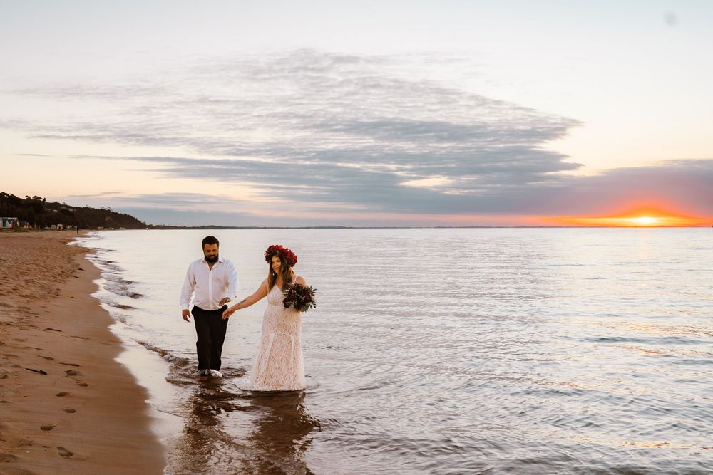 Two people dancing and splashing in the ocean at sunset along a scenic beach shoreline.