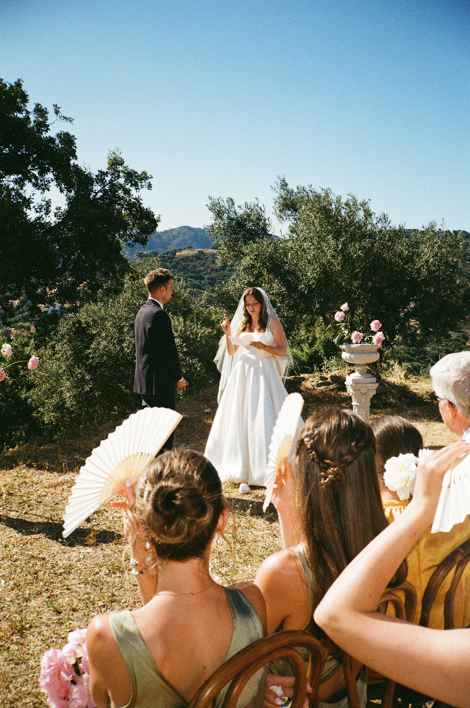 A cheerful wedding party celebrates on the grounds of a historic stone manor house in muted sepia tones.