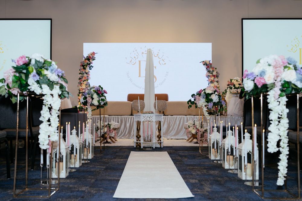 Indoor wedding ceremony setup with white floral arch, lanterns, and rose petals lining the aisle to the altar.