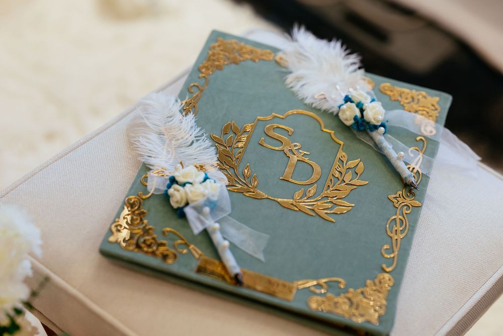 Elegant teal and gold wedding guest book decorated with white feathers and floral embellishments.
