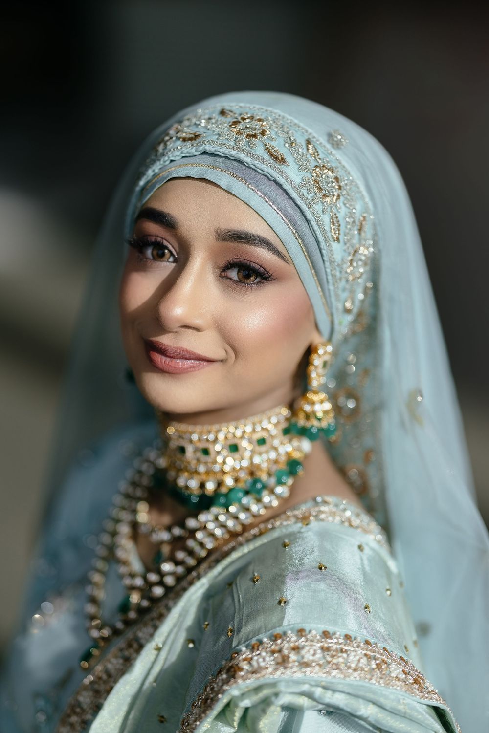 Traditional South Asian bride wearing a light blue embroidered hijab and ornate pearl jewelry for her wedding day.