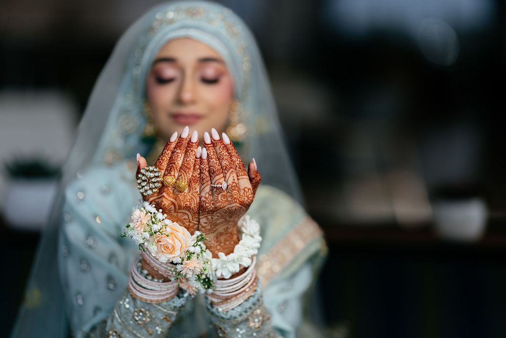 A bride in traditional Islamic attire with henna-decorated hands raised in prayer during a wedding ceremony.