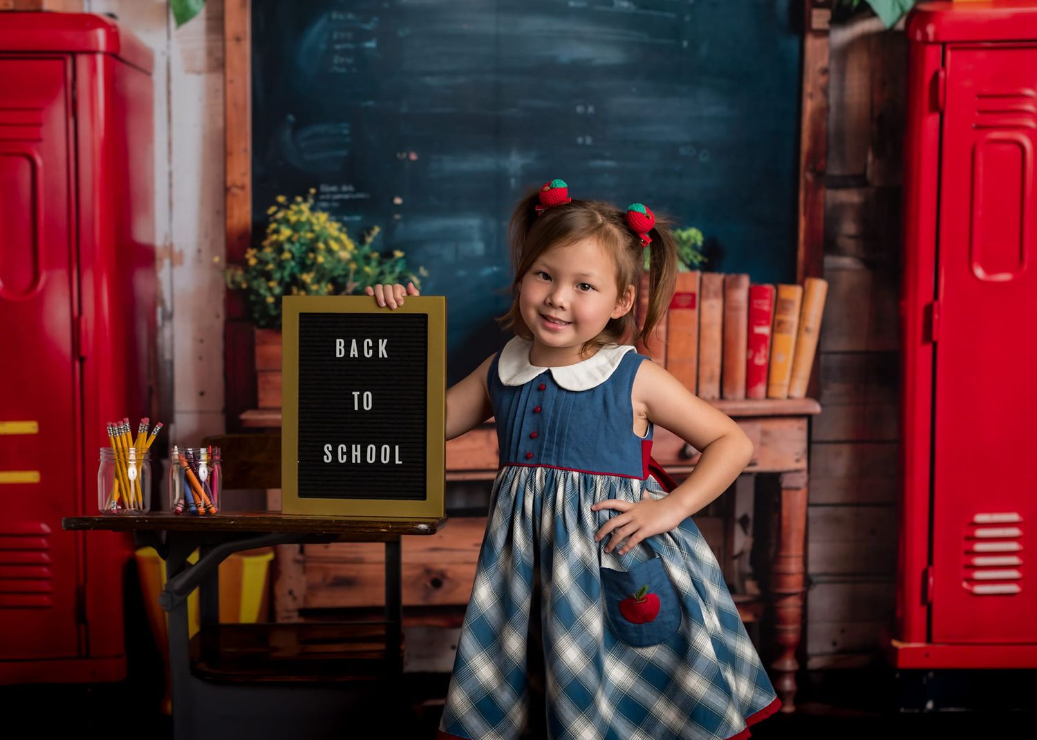 A child stands in front of a chalkboard back-to-school scene with red lockers and books in the background.
