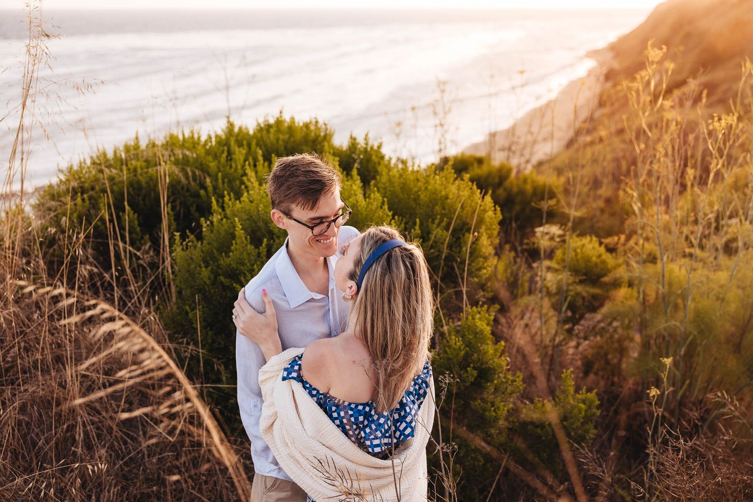 A couple shares a tender moment against the backdrop of Ellwood Bluffs and Ellwood preserve beach at sunset, creating a romantic silhouette.