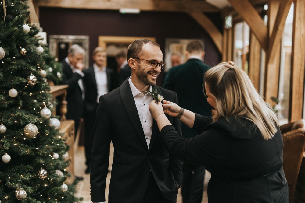 A couple shares a festive moment beside a decorated Christmas tree in an elegant wooden interior venue.
