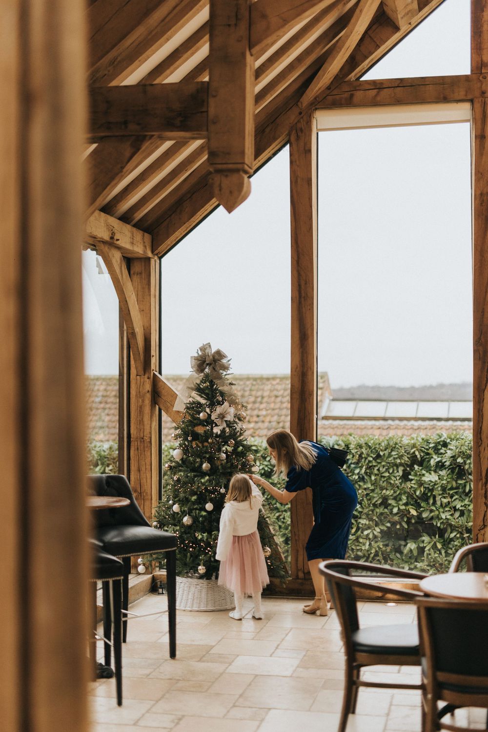 A rustic covered patio with wooden beams frames a view of the countryside through large glass windows.