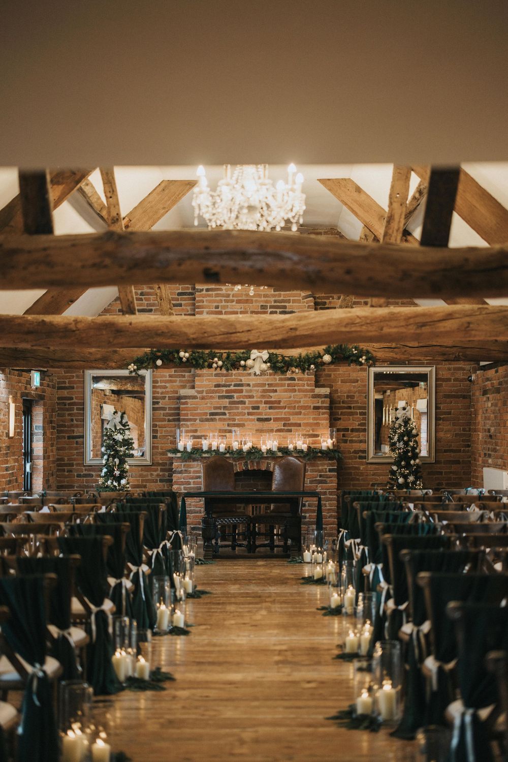 Rustic wedding venue interior with exposed brick walls, wooden beams, and elegant chandeliers creating ambient lighting.