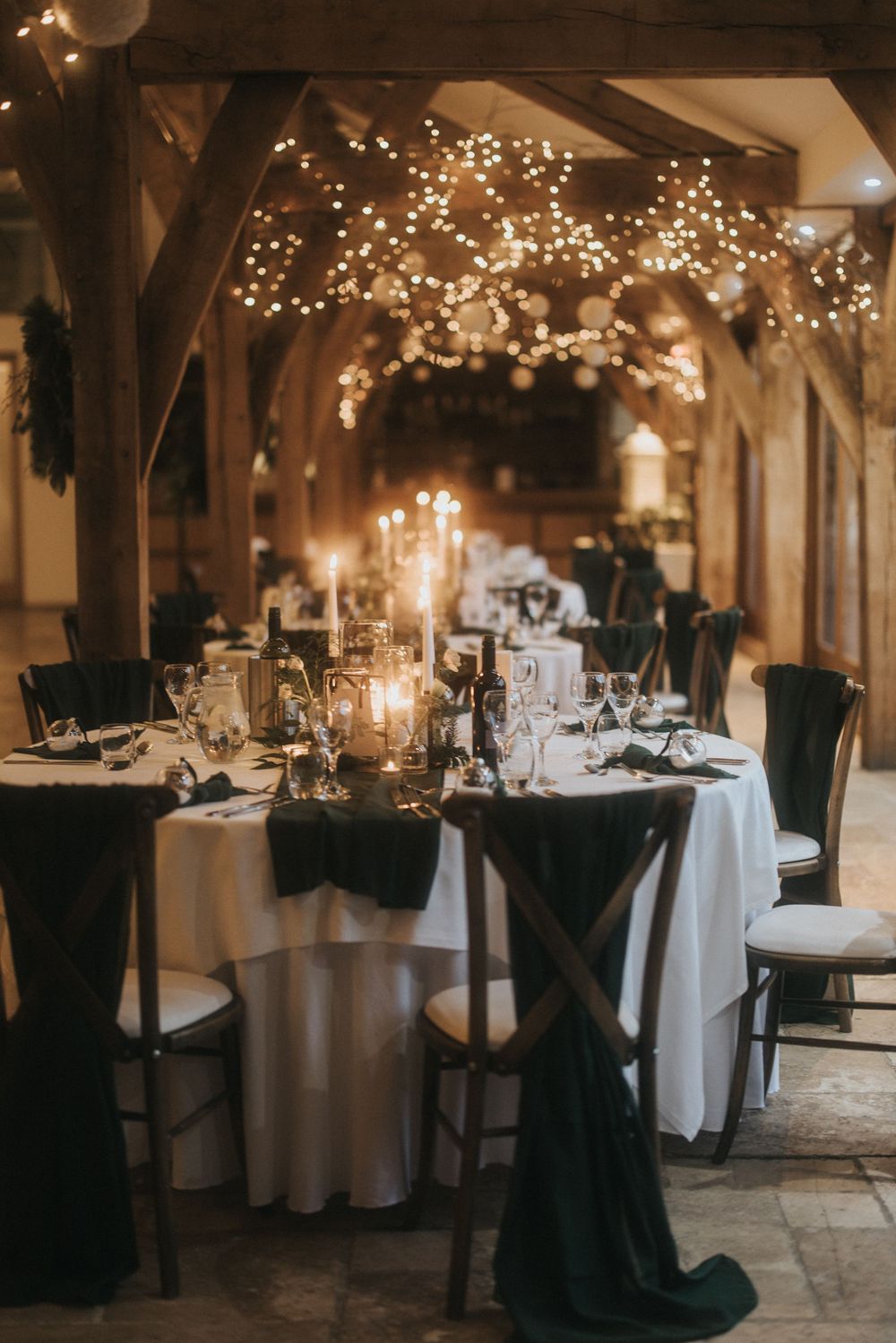 Elegant wedding reception venue with moody lighting features round tables adorned with crisp white linens and twinkling lights above.