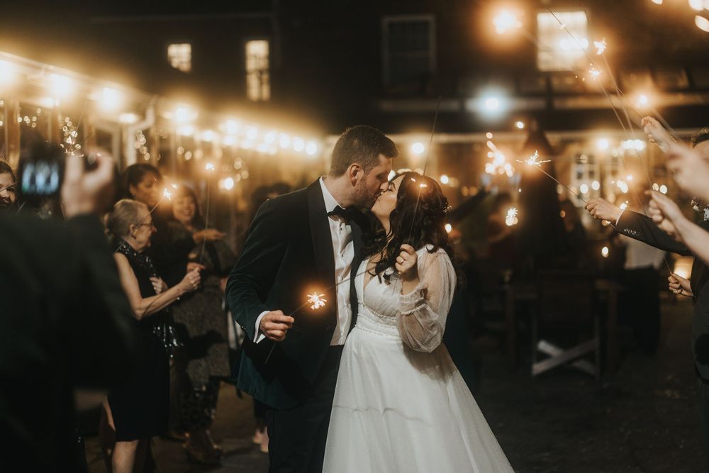 Wedding couple dances together under romantic string lights at an evening outdoor reception.