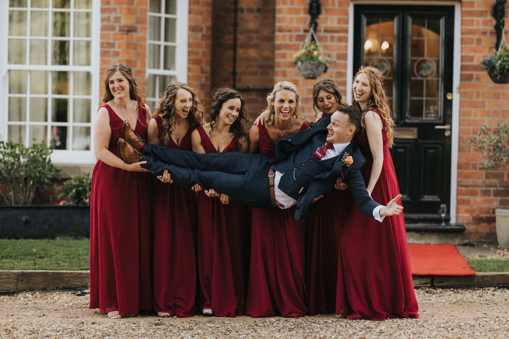 Wedding party members in burgundy dresses gather together outside a brick building for a group photo.