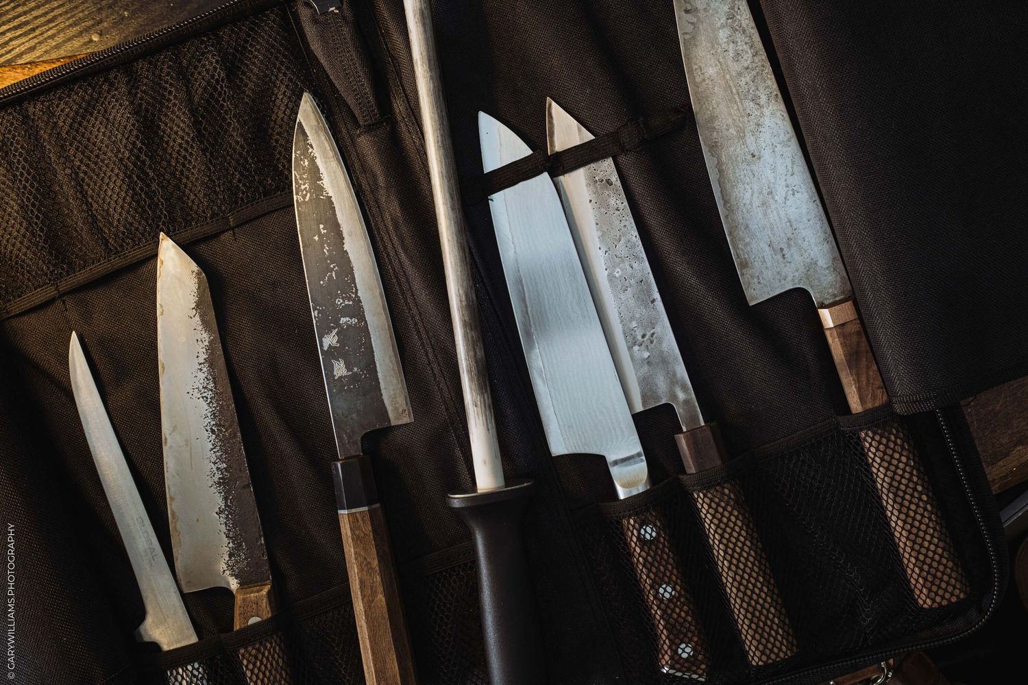 Professional kitchen knives with wooden handles arranged in a dark rustic display against a shadowy background.
