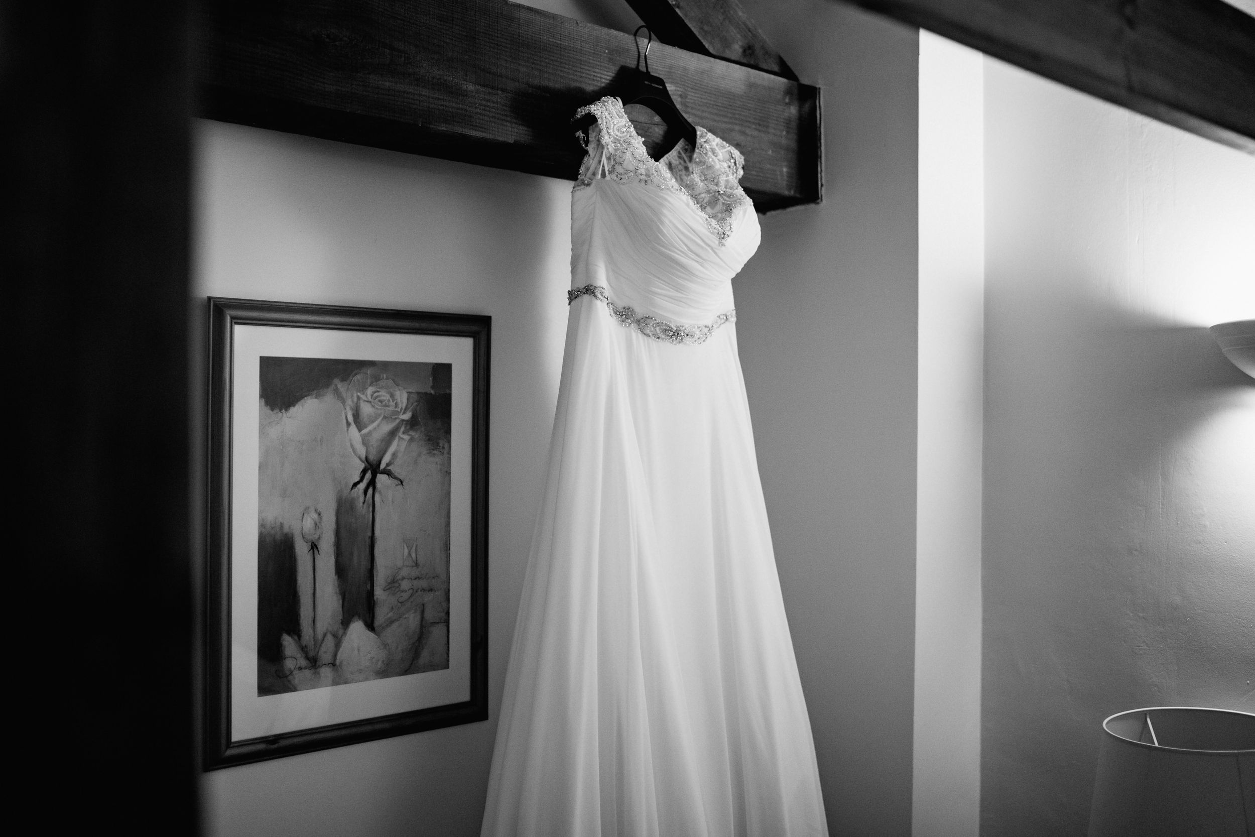 White wedding dress hanging against grey wall with black and white artwork.