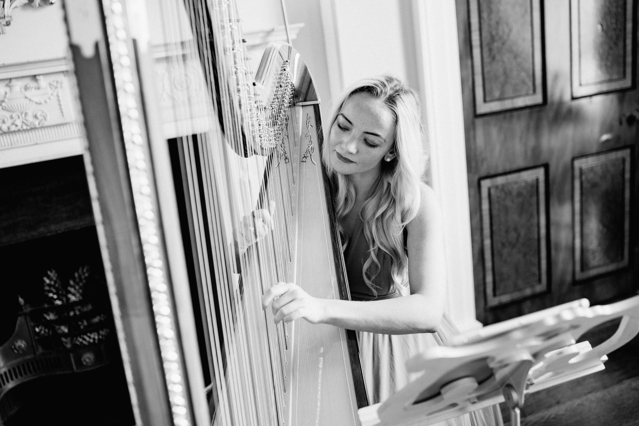 A harpist performs on an ornate classical harp in a formal interior setting.