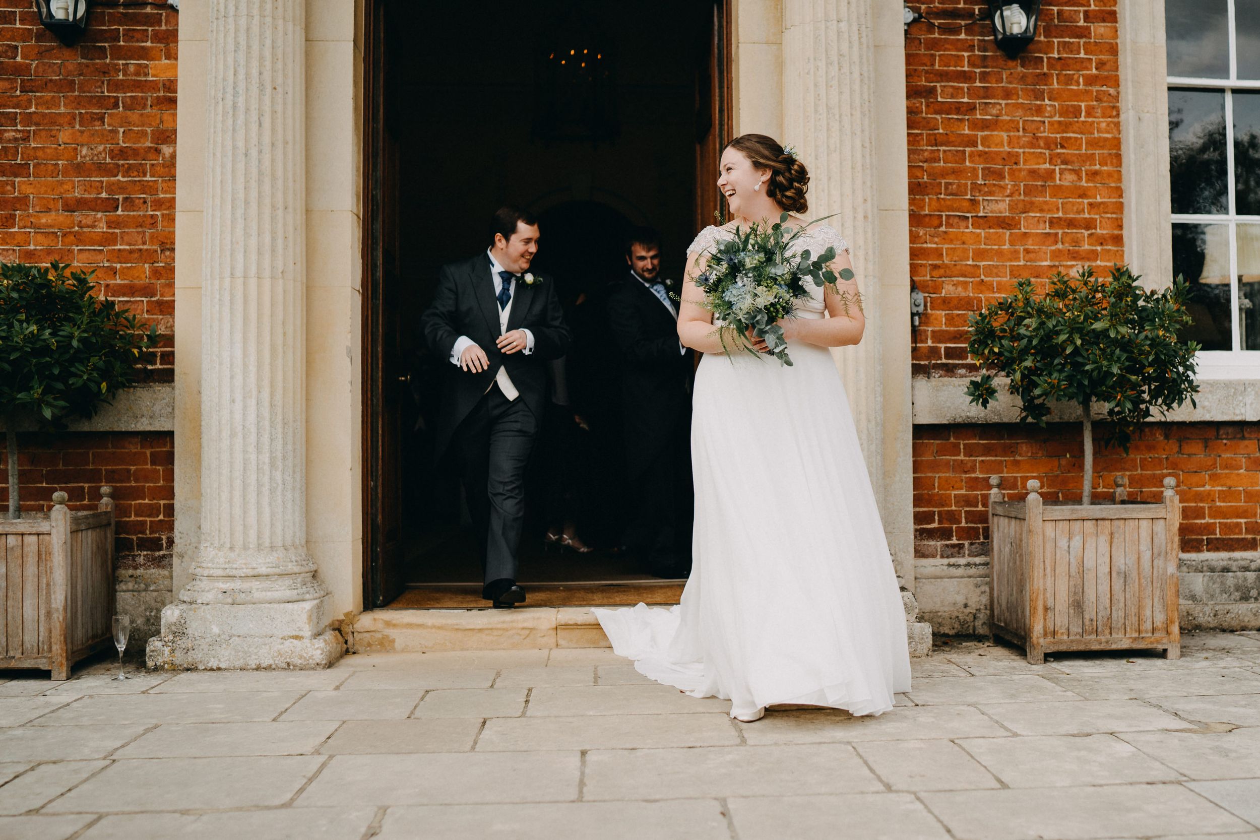 An elegant wedding scene outside a brick building with white columns and decorative planters.