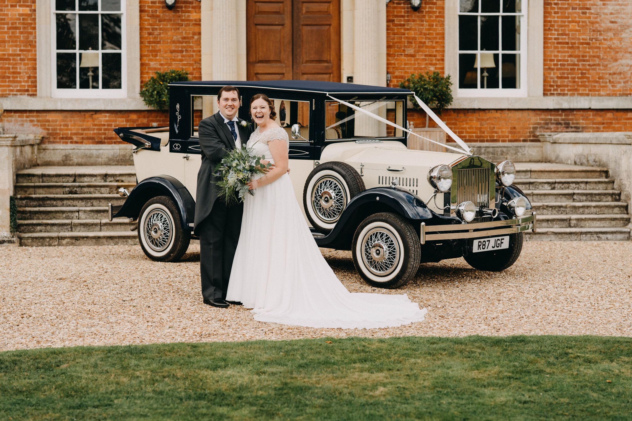 A classic vintage wedding car parked in front of a stately brick mansion.