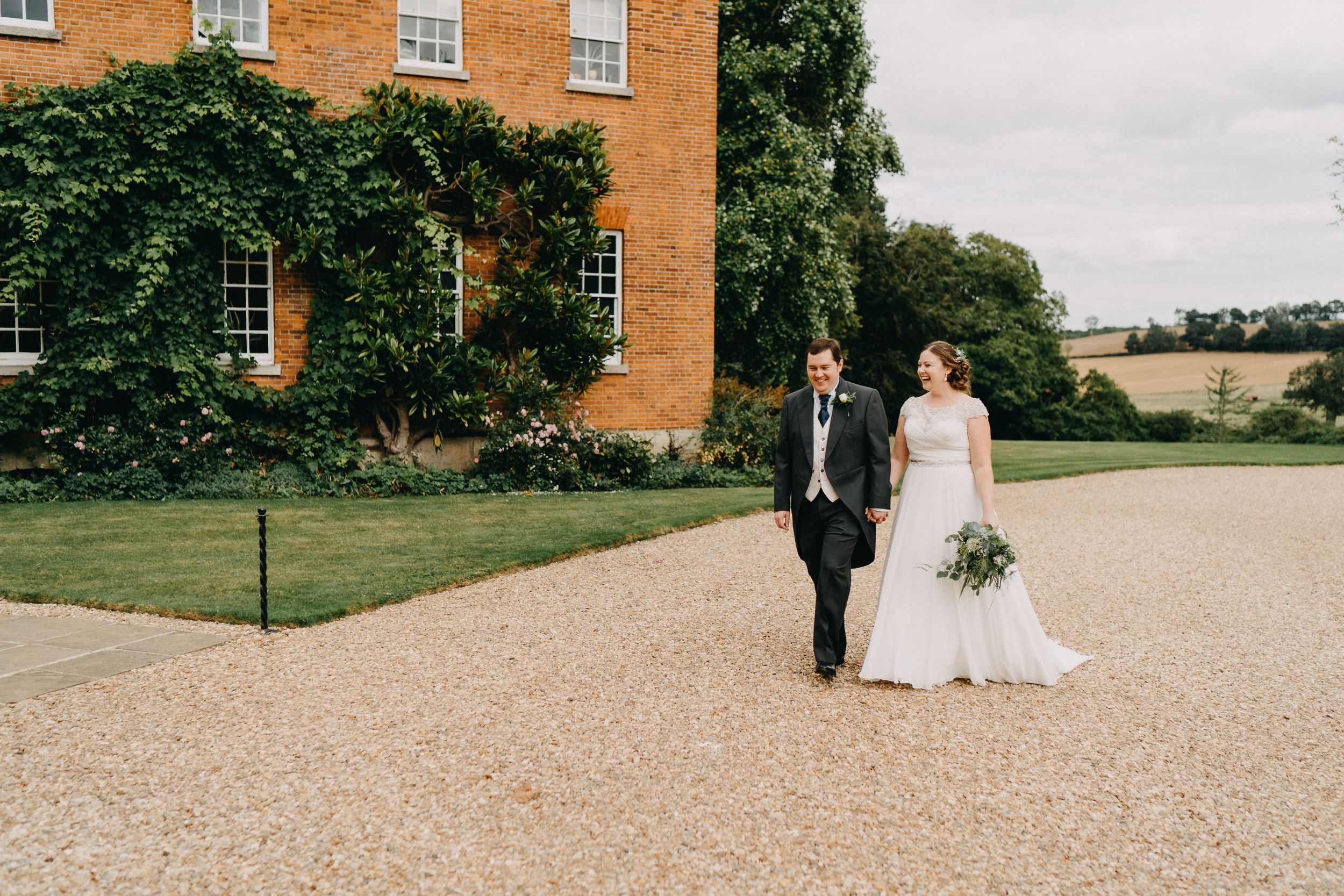 Wedding couple posed in front of a historic ivy-covered building with orange brick walls.