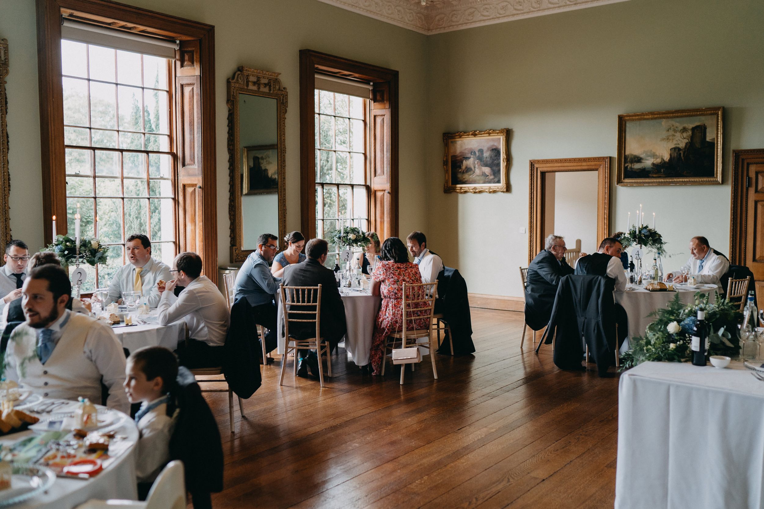 Elegant dining room at Kelmarsh Hall filled with wedding guests enjoying a reception meal.