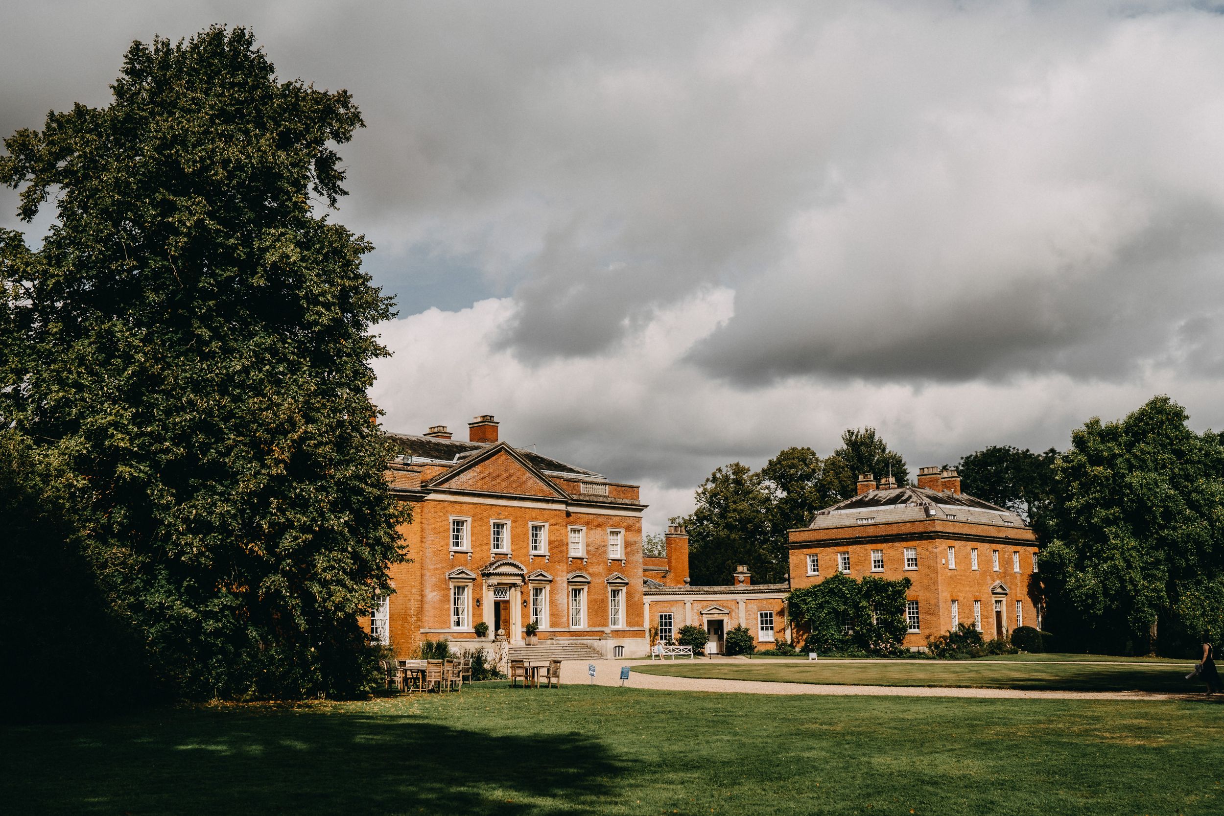 Kelmarsh Hall Stately orange brick mansion with manicured grounds under dramatic cloudy sky.