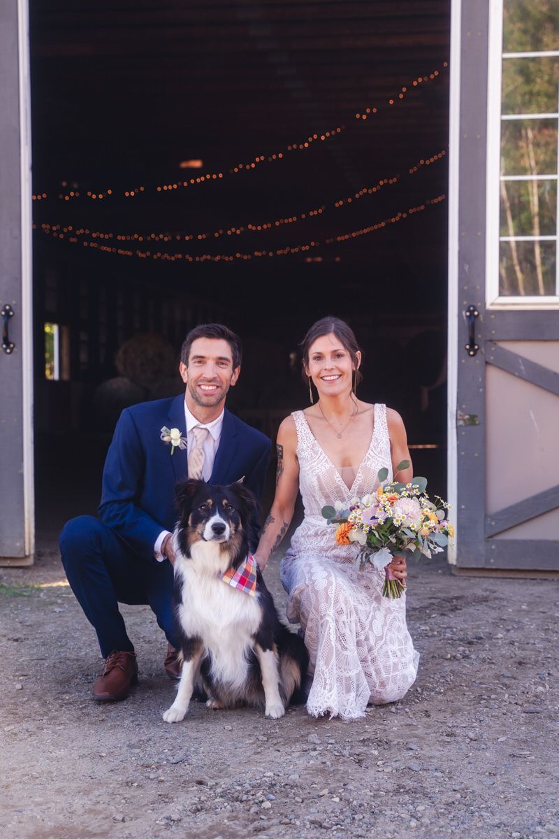 A bride and groom kneel down to pose with their Australian Shepherd for their first married family portrait.