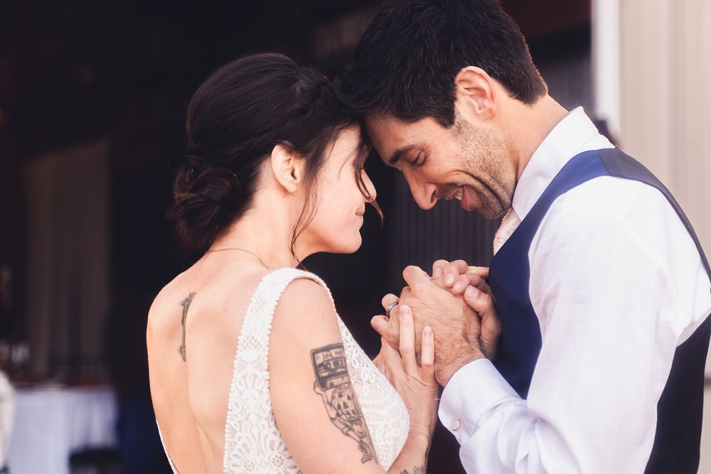 A wedding couple faces each other with hands clasped together at the end of their first dance.
