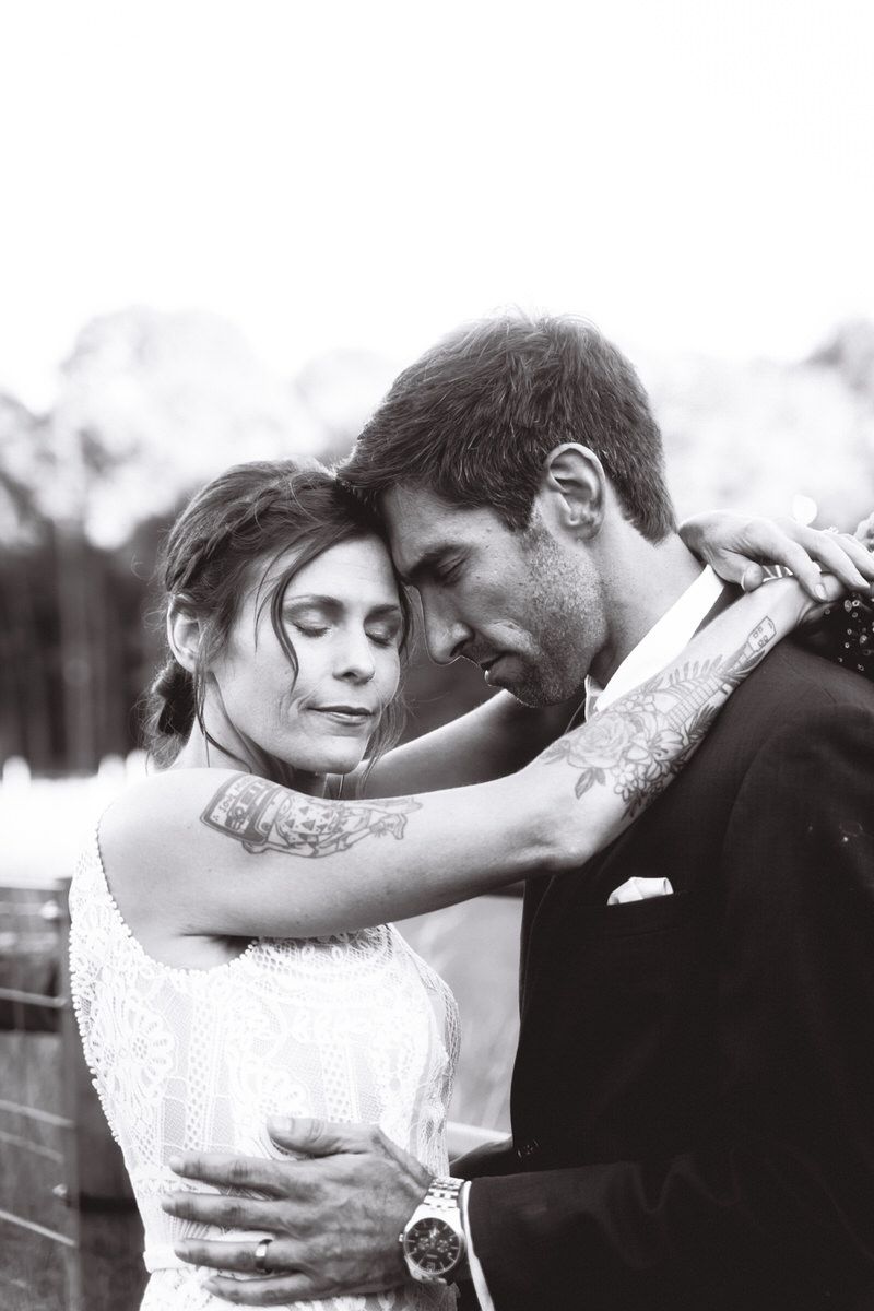 A black and white photo of a bride and groom leaning gently towards one another, posed against a fence during their portrait hour.