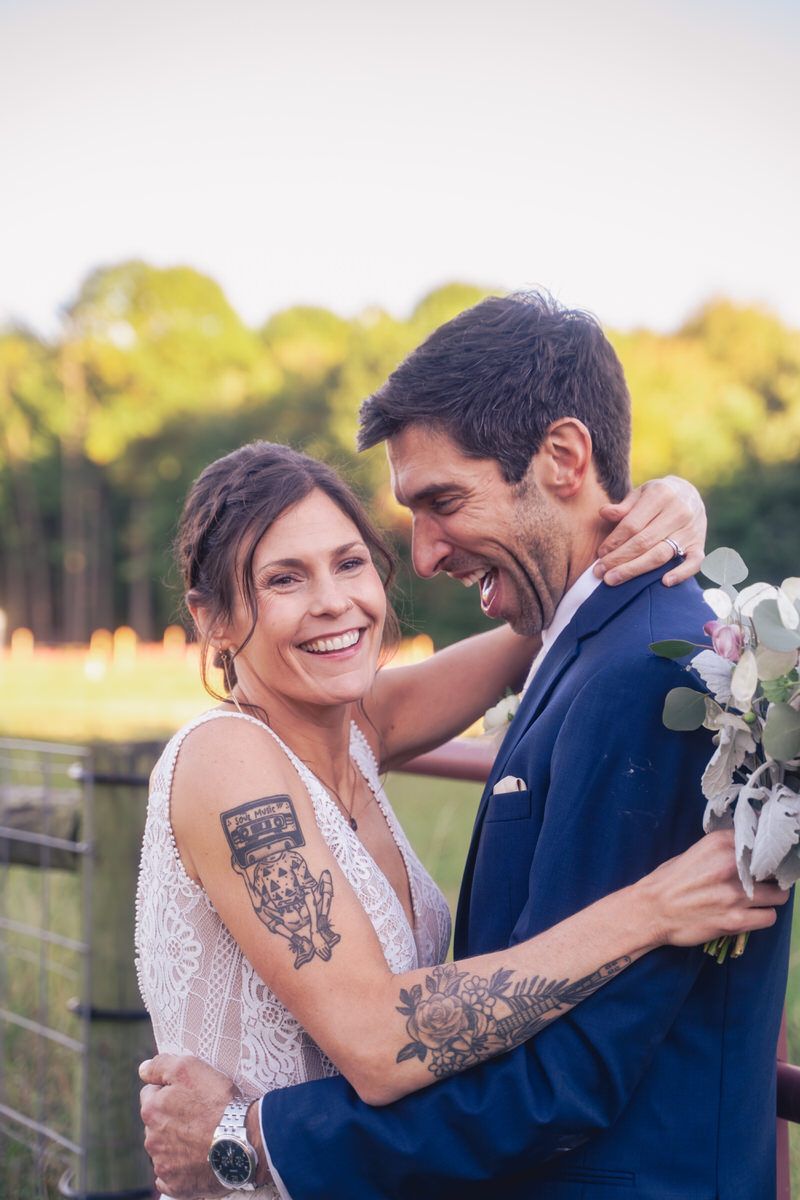 The bride and groom laugh together as they lean against a fence during their portrait hour.