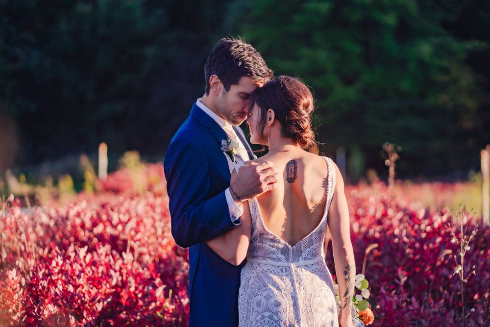 A bride and groom stand before a vibrant field in October at wedding just before sunset.