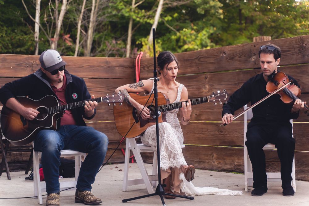 Holding a pick in her mouth, the bride plays guitar to entertain her wedding guests at her laid-back DIY, intimate reception event.