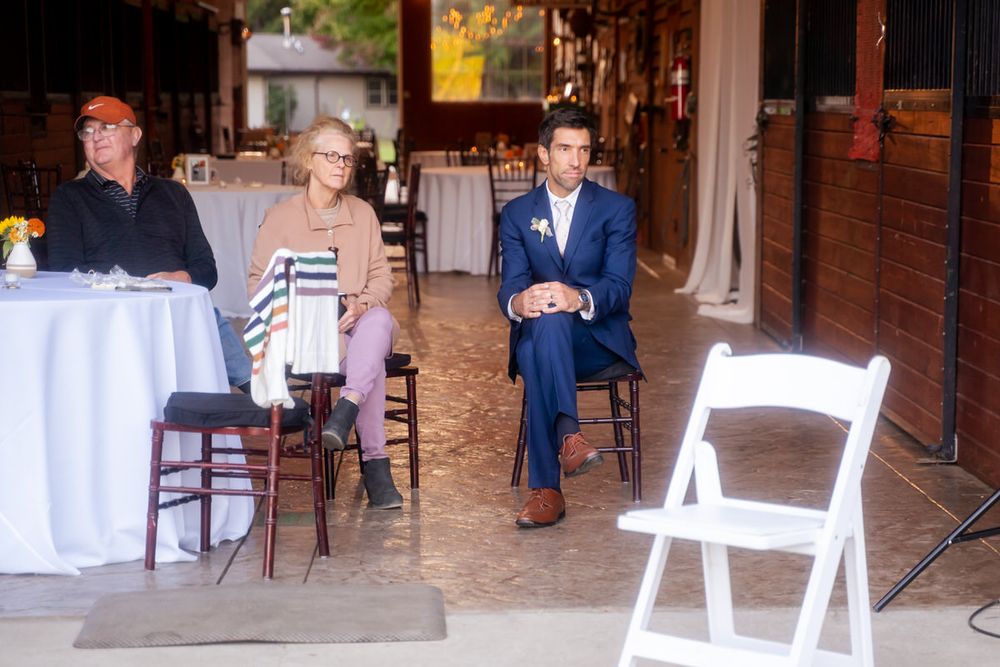The groom listens as the bride plays guitar to entertain her wedding guests at her laid-back DIY, intimate reception event.