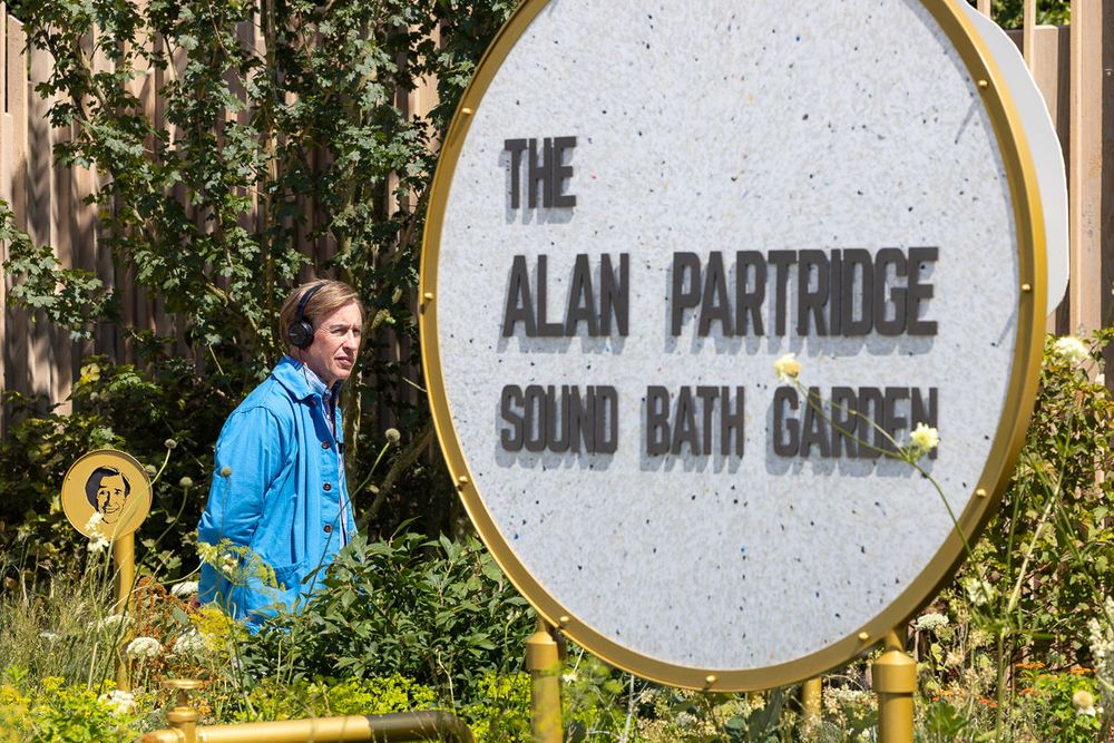 A white circular sign reading 'The Alan Partridge Sound Bath Garden' with Alan Partridge and the garden in the background.