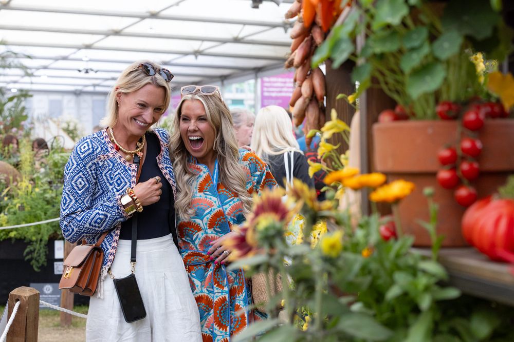 A couple browses through fresh vegetables and flowers at a garden market greenhouse display with colorful produce.