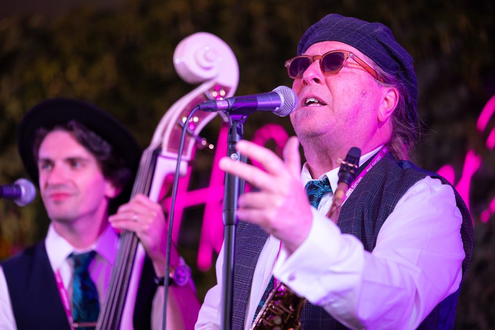 Musicians performing on stage with pink lighting effects in the background during a live concert.