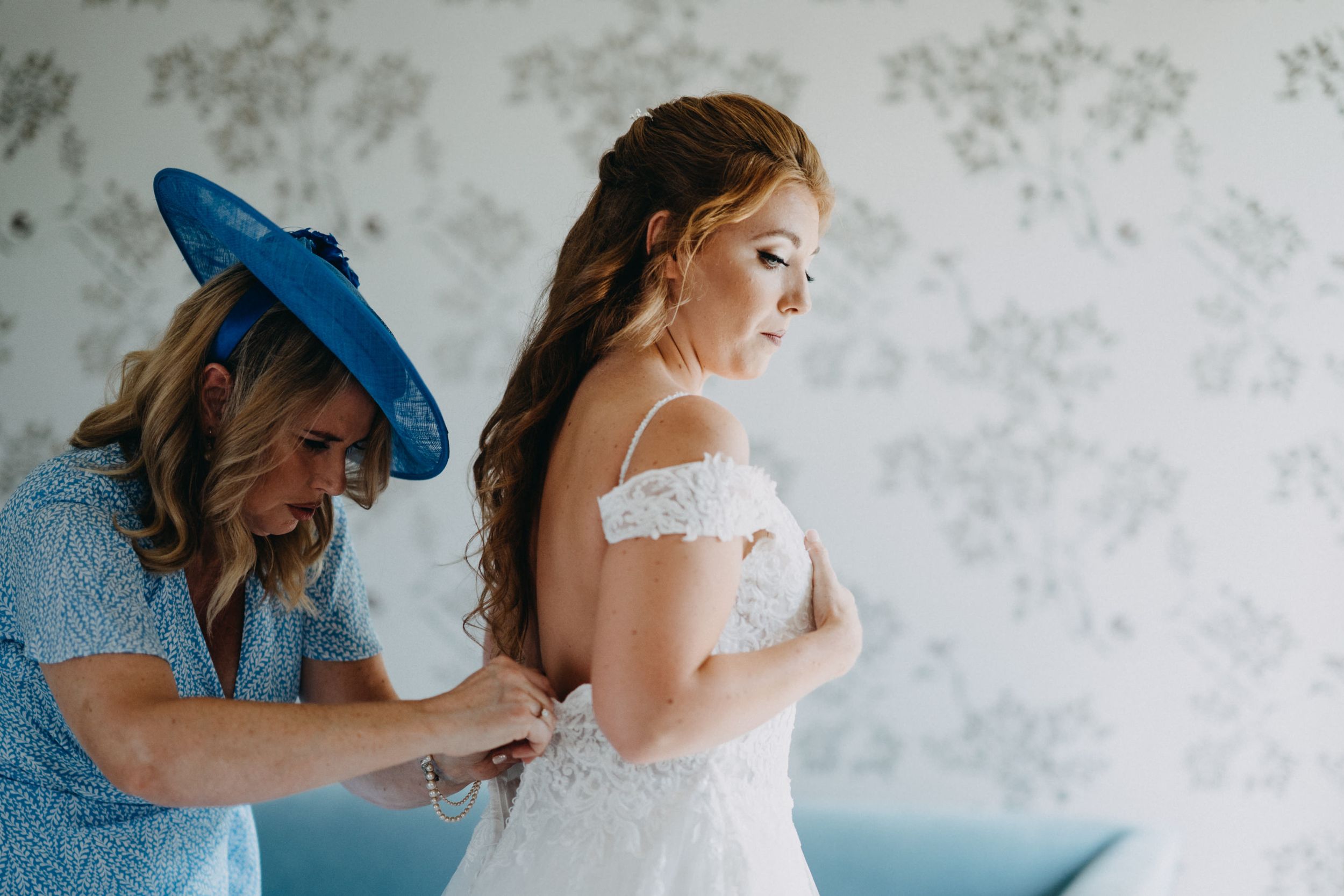 Helpers assisting with the final touches of a white lace wedding dress.