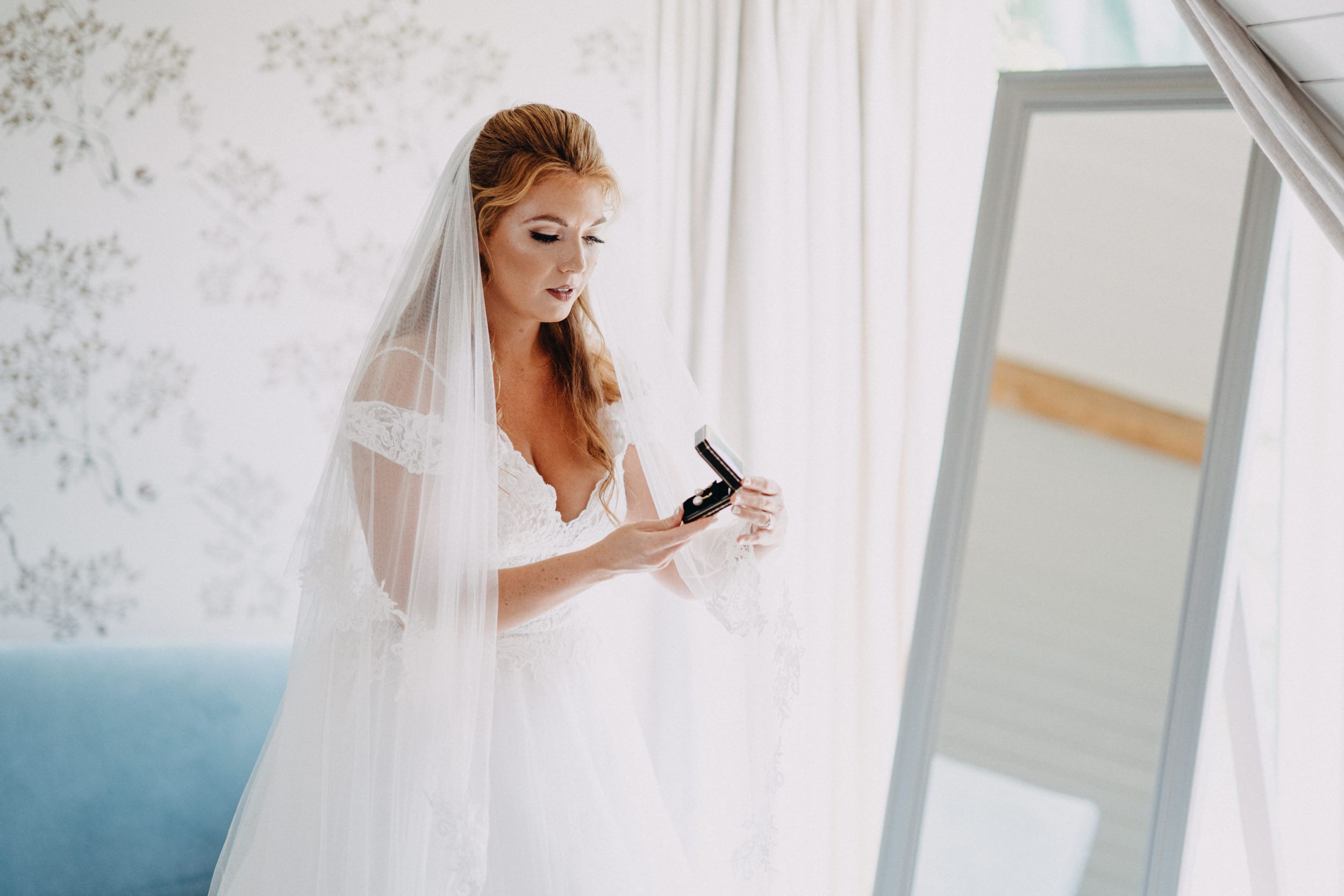 Bride in white wedding gown and veil applies makeup while getting ready, South Farm Cambridgeshire.