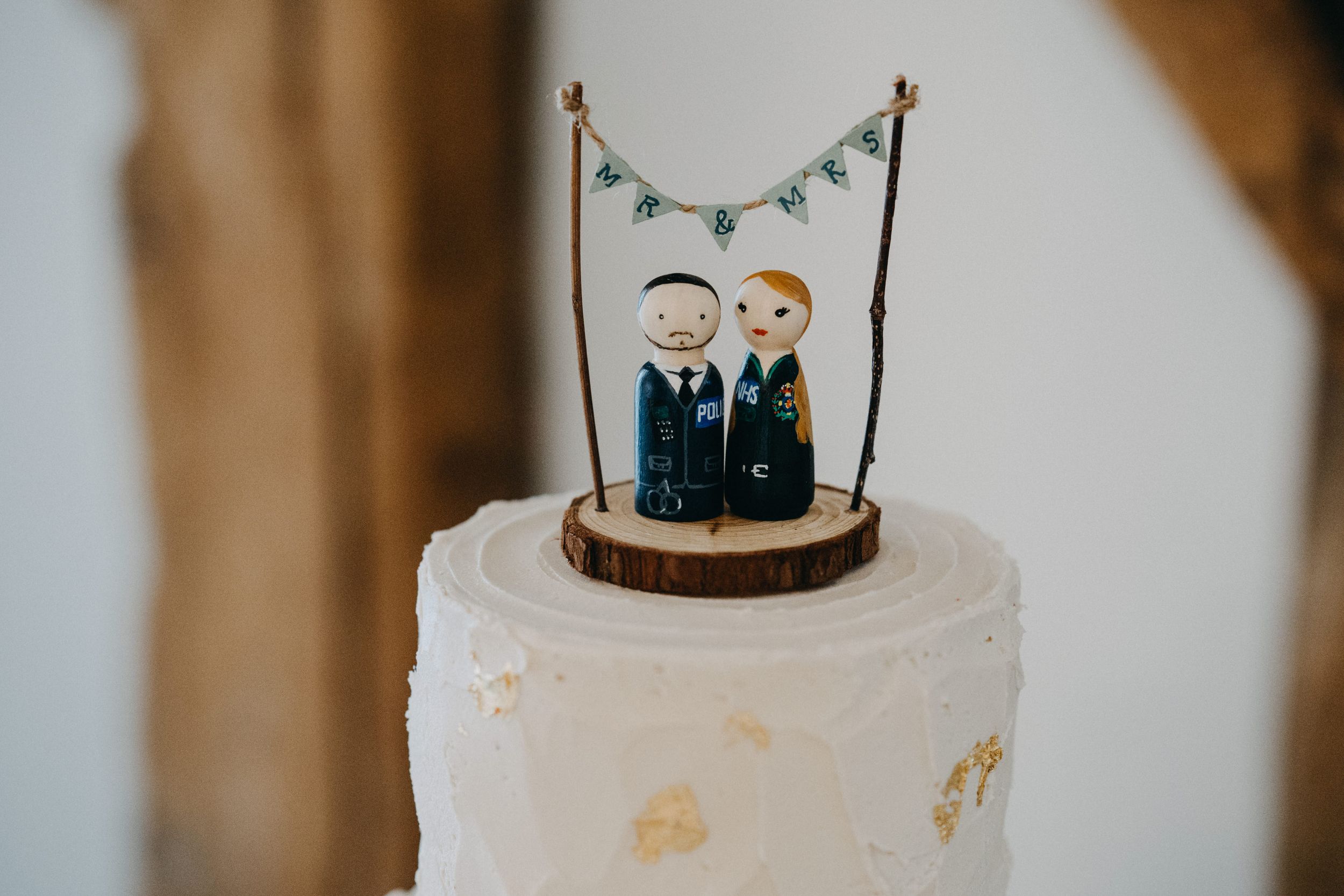 White wedding cake topped with custom figurine cake toppers and delicate blue bunting decoration.