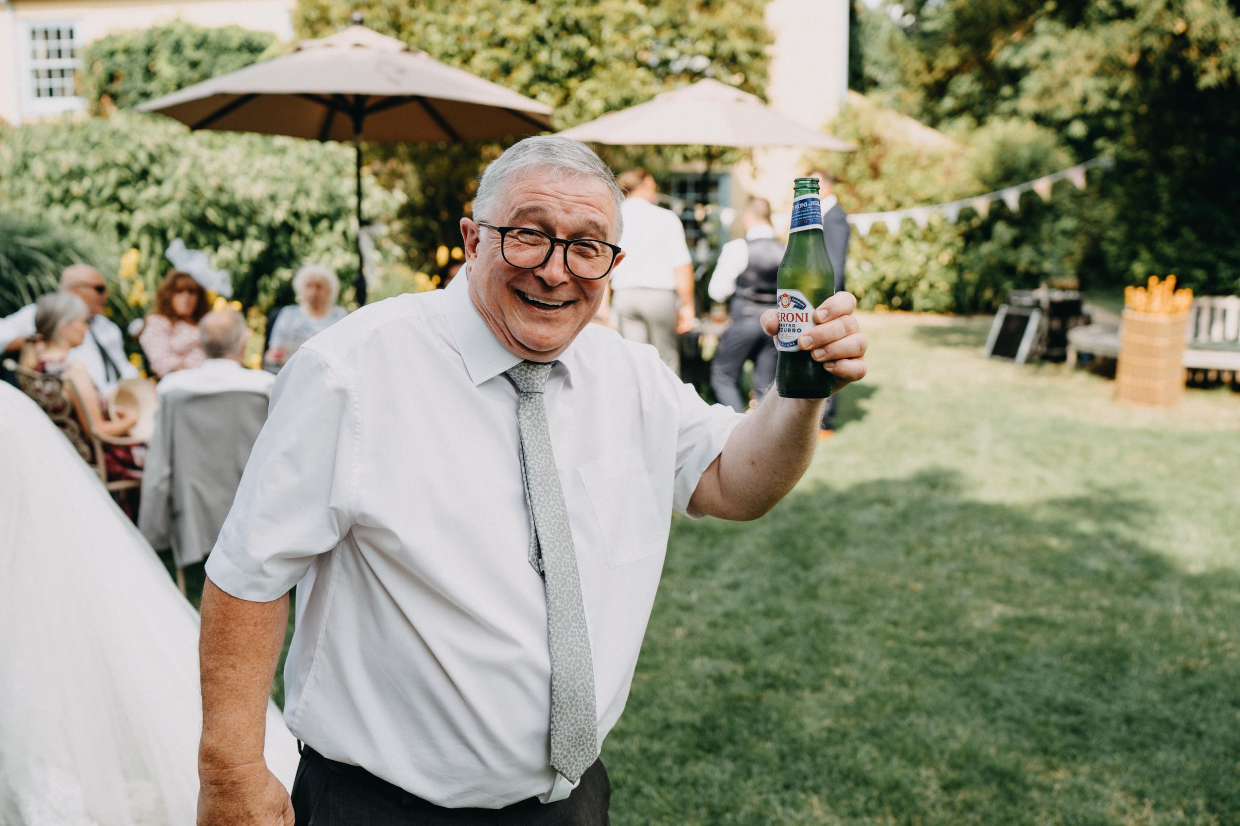 Guest in white shirt and tie enjoying outdoor wedding reception on sunny lawn.