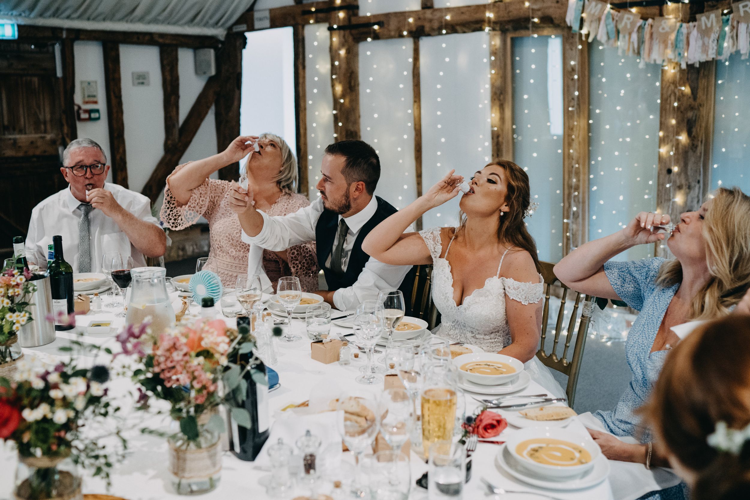 Wedding party toasting and laughing together at decorated reception table.