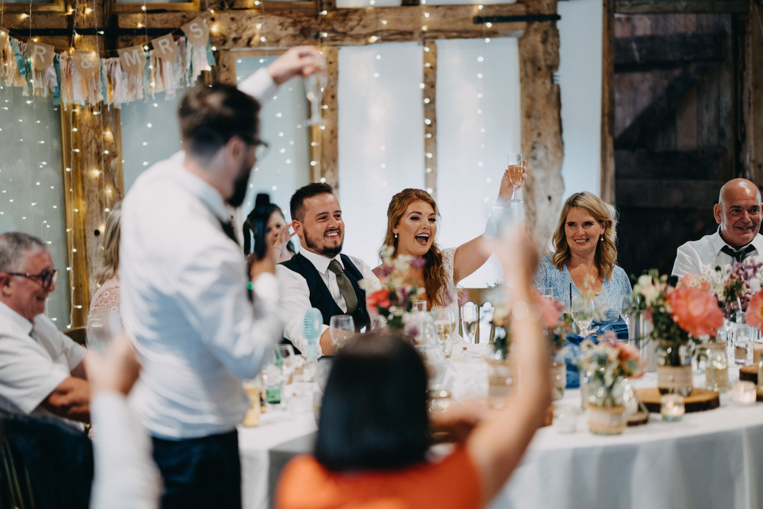 Wedding reception guests raising glasses in celebratory toast at decorated venue.