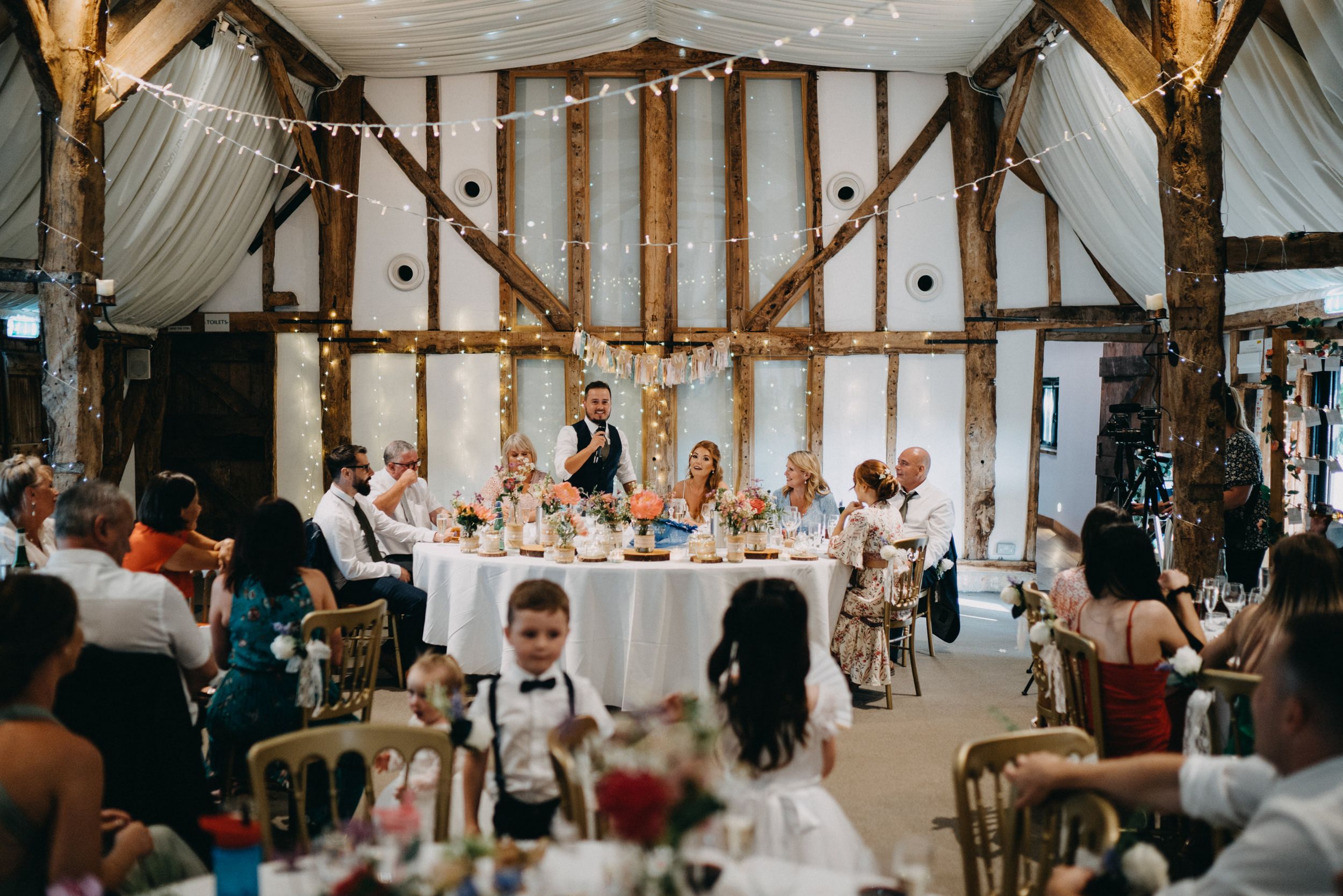 Wedding reception in progress inside rustic barn at South Farm with exposed beams and string lights.