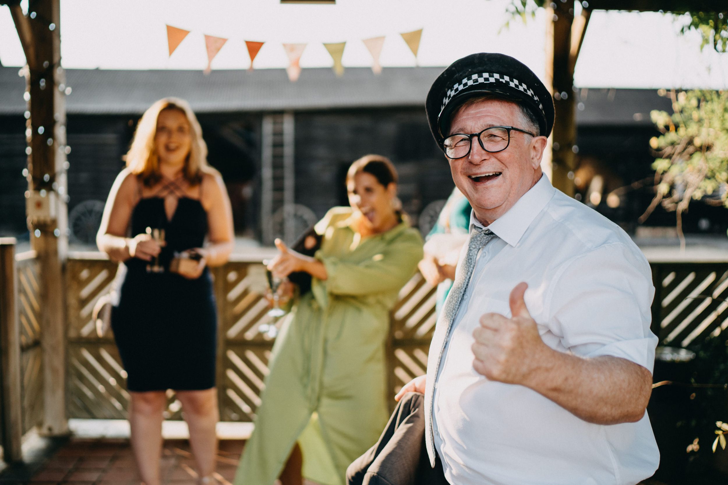 Guest giving enthusiastic thumbs up at outdoor wedding party with bunting decorations.