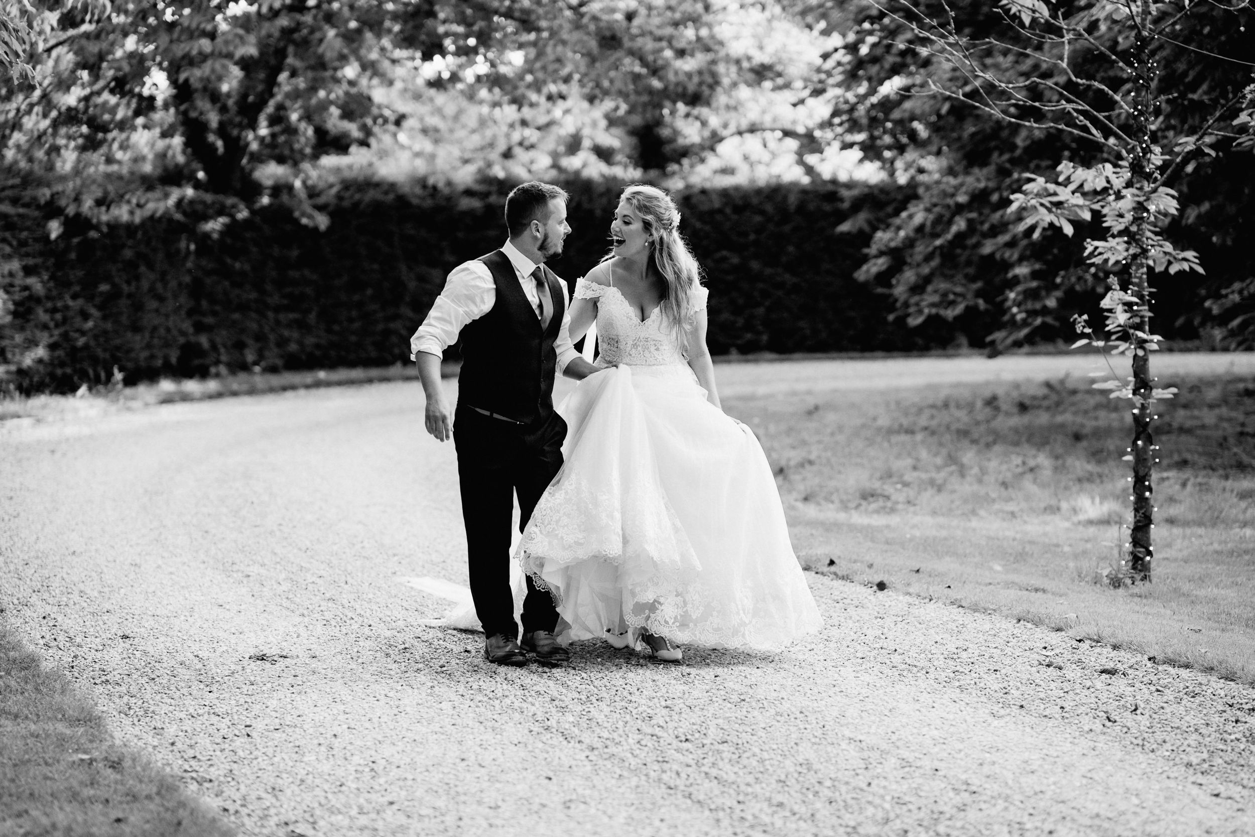 Black and white photo of a wedding couple walking together on a path surrounded by greenery of South Farm.