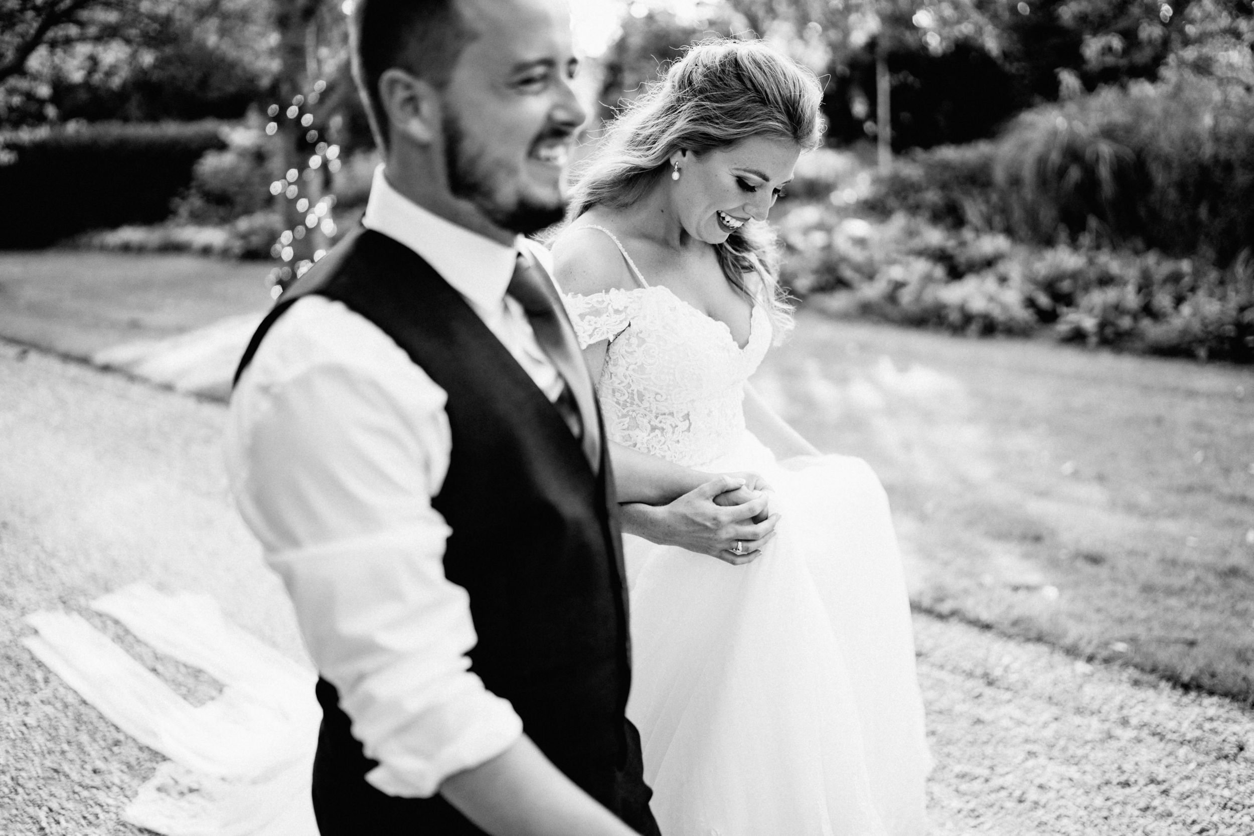 Elegant black and white portrait of a couple in wedding attire sharing a tender moment in a garden setting.