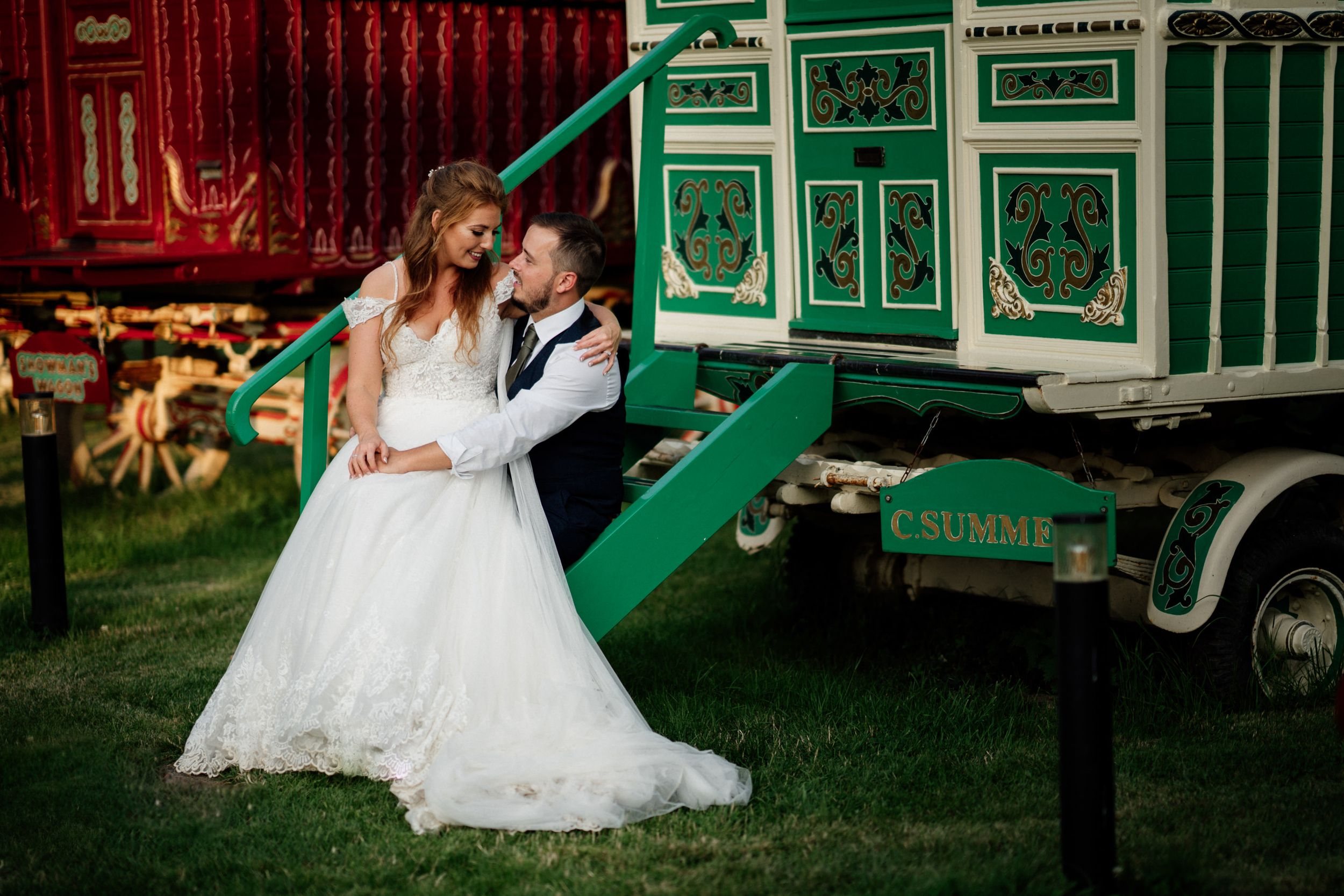 Wedding couple poses romantically by vintage green carnival wagon at South Farm.