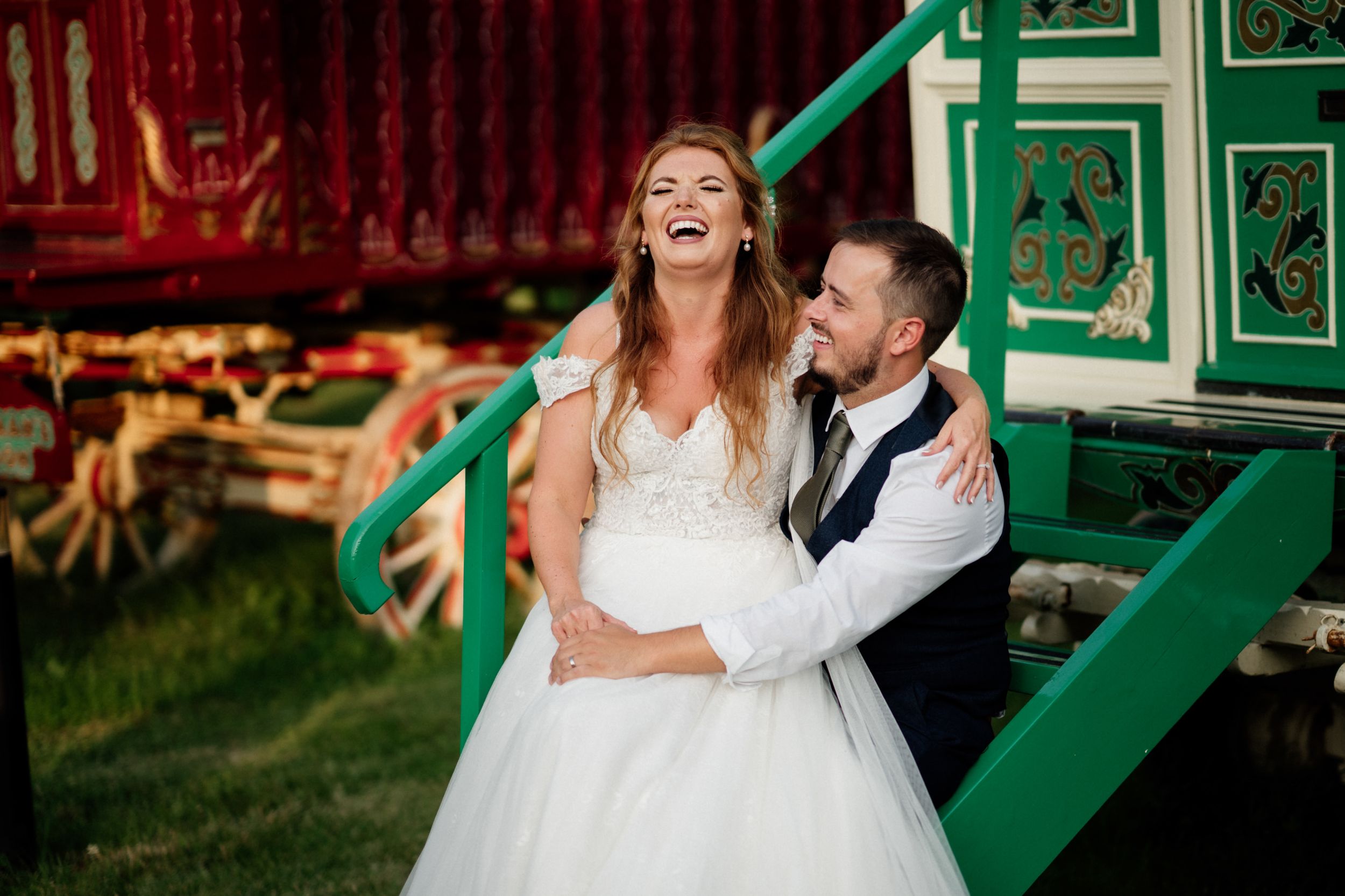 Joyful wedding couple shares a candid laughing moment by vintage carnival equipment.