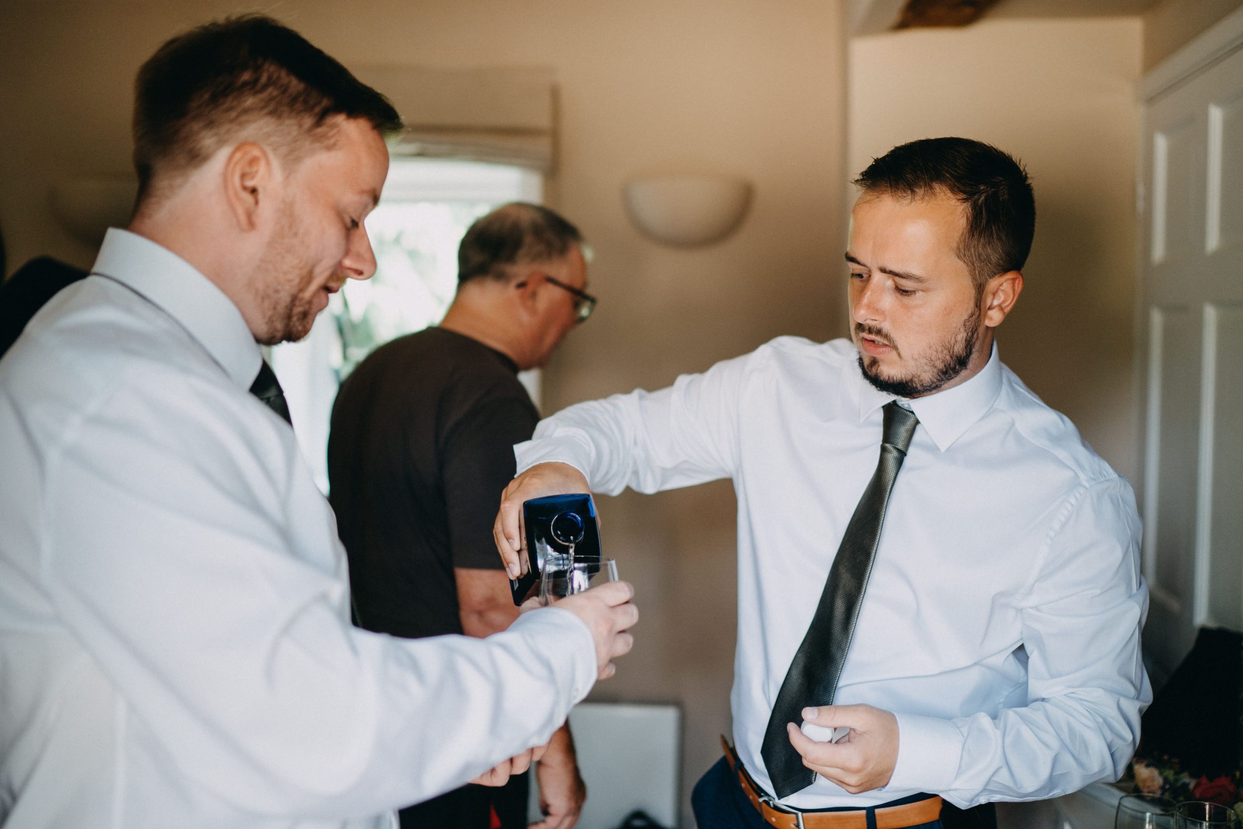 Groomsmen in white shirts and ties sharing a drink while getting ready.