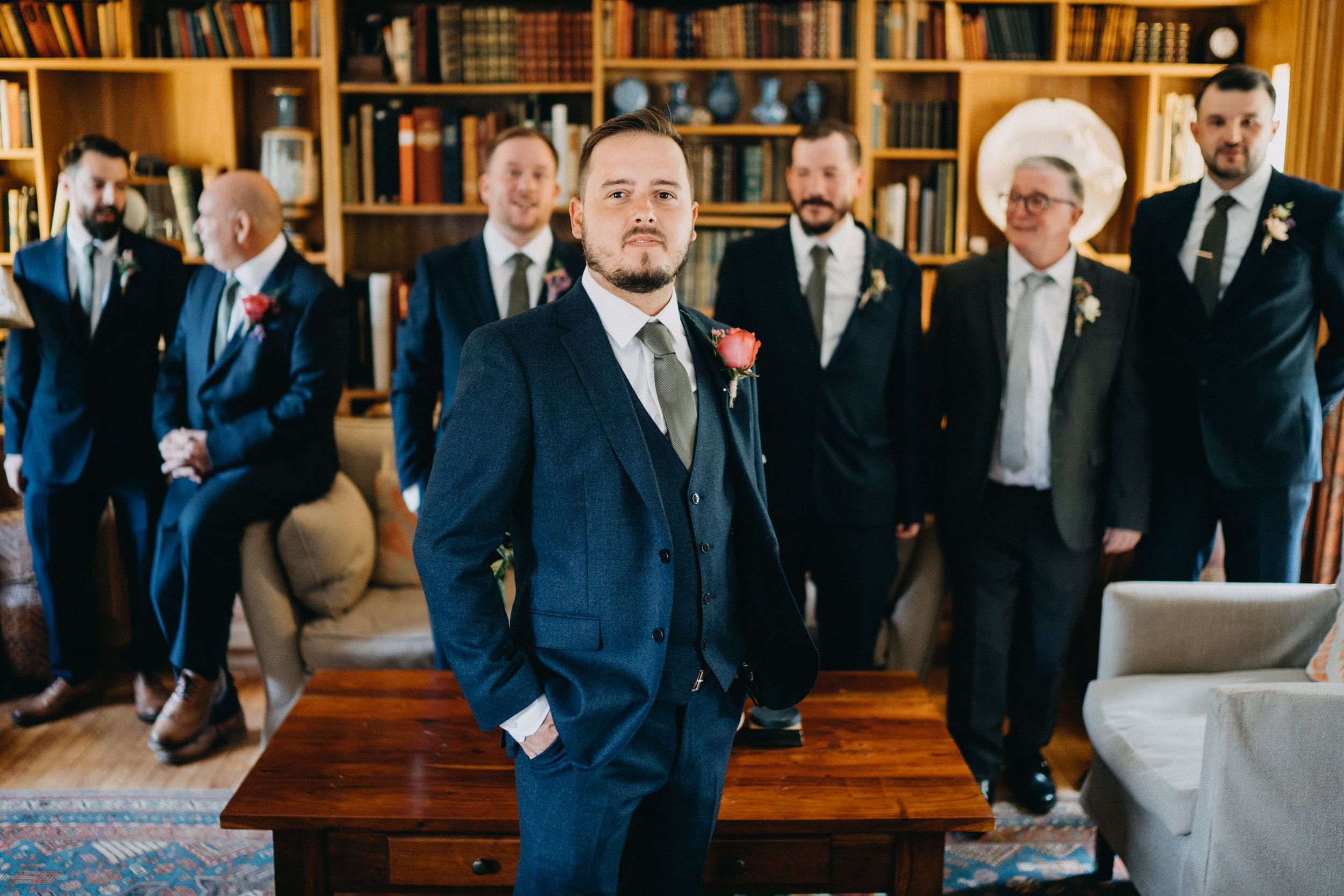Groom and groomsmen in navy suits pose in an elegant library setting.