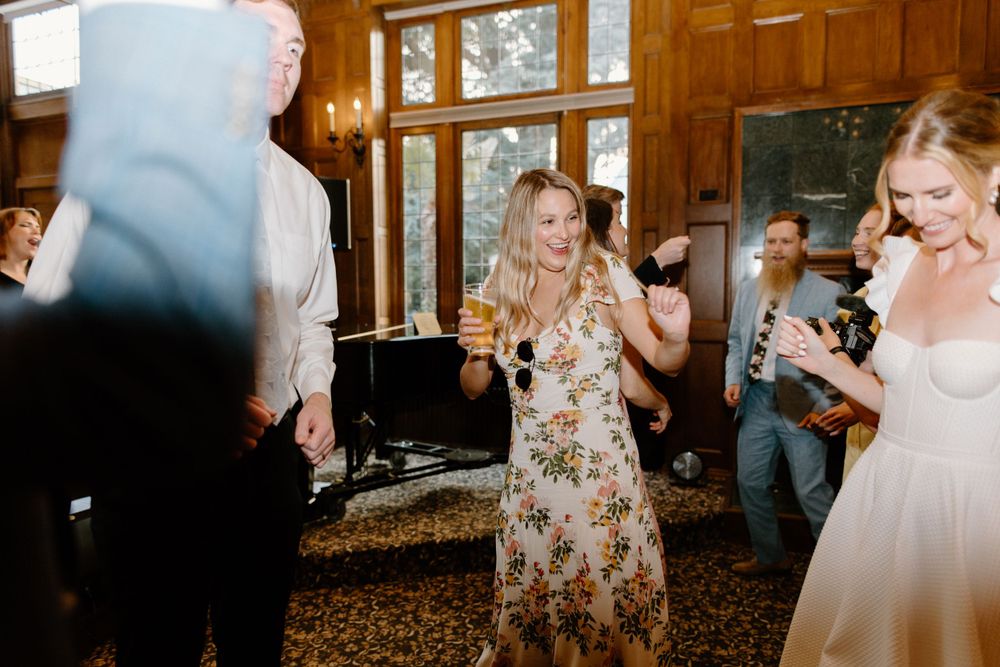 Wedding guests dancing and celebrating in a rustic venue with large windows and natural light.