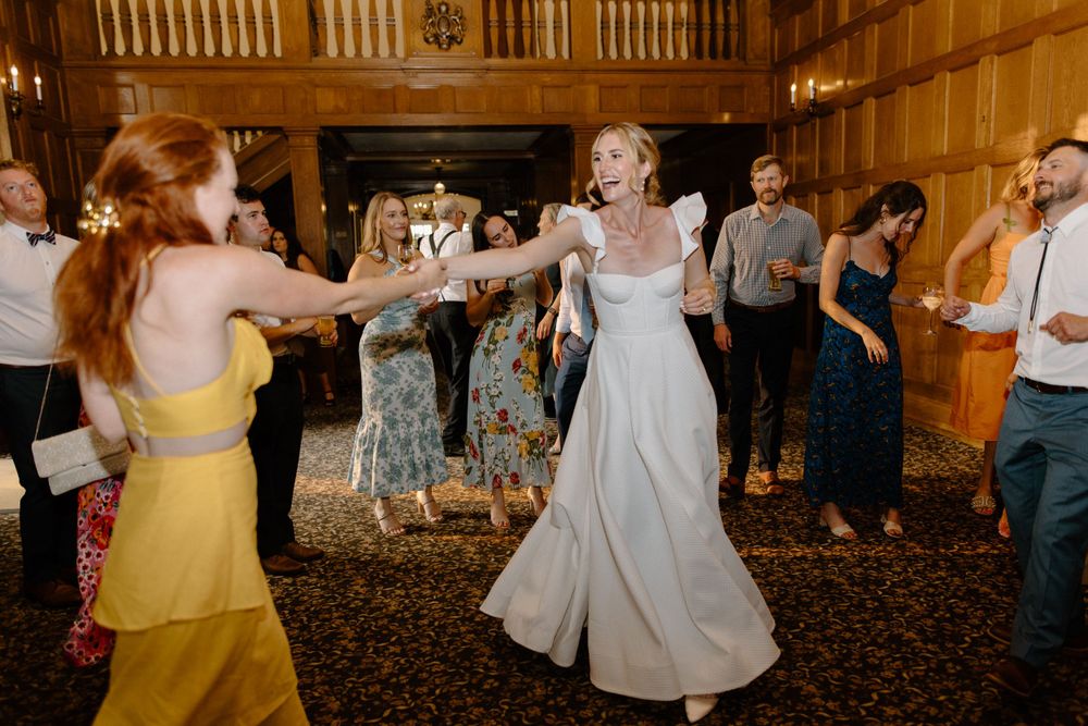 People dancing joyfully at an indoor wedding reception with warm wooden walls and carpeted floor.